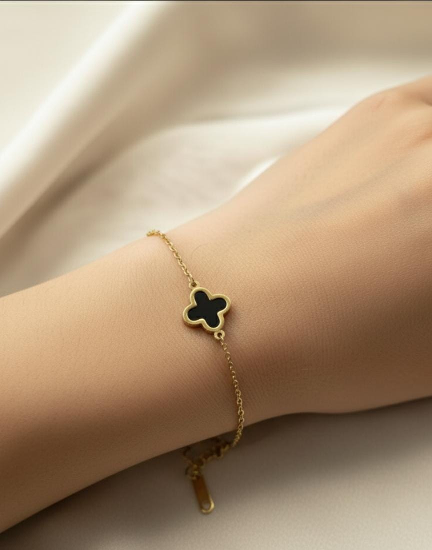 Gold bracelet with a clover-shaped charm on a wrist against a neutral background