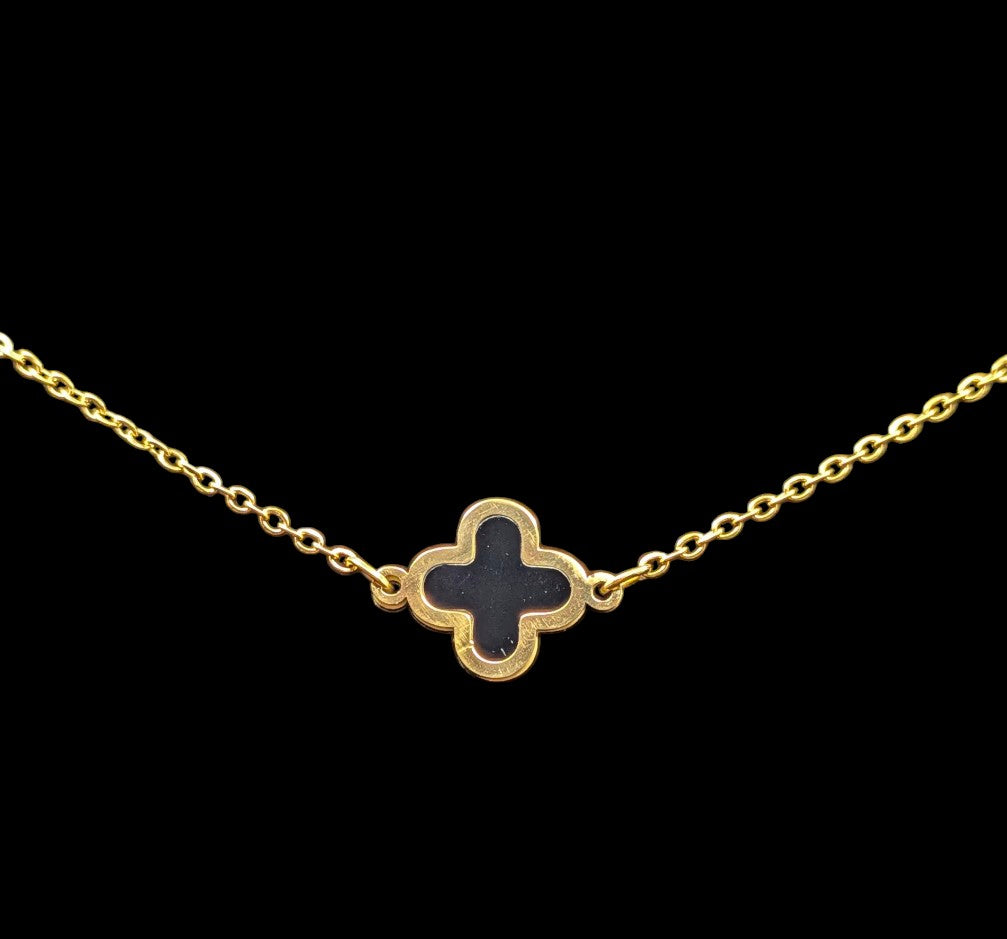 Gold toned bracelet with a black clover-shaped pendant on a black background