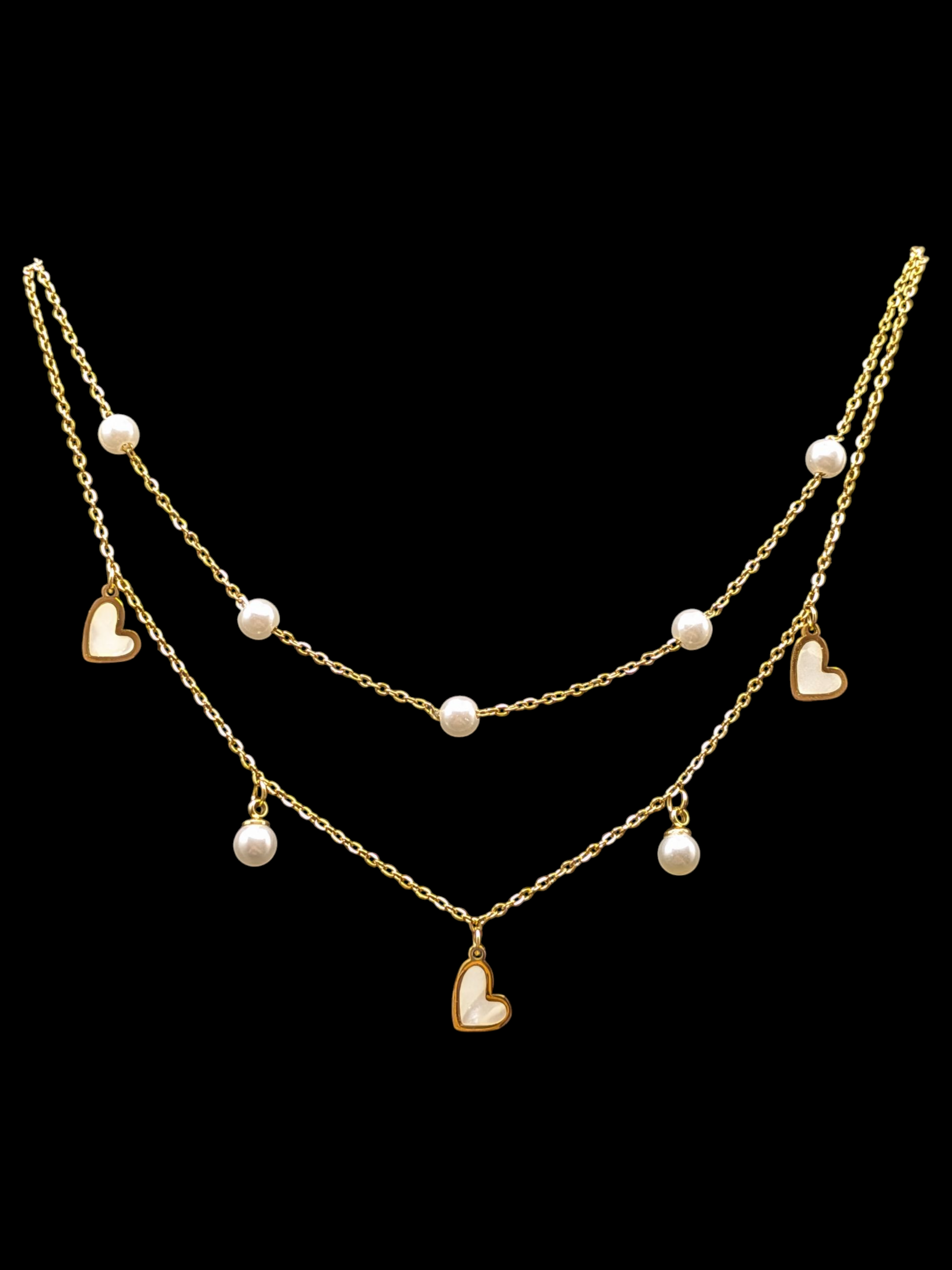 Gold tone necklace with heart and pearl pendants on a black background